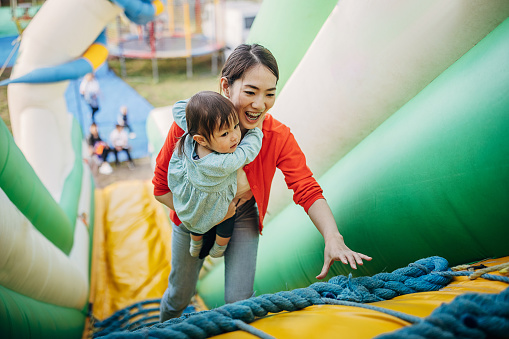 Two people, Japanese woman with her little daughter having fun on an inflatable bouncy castle in amusement park.