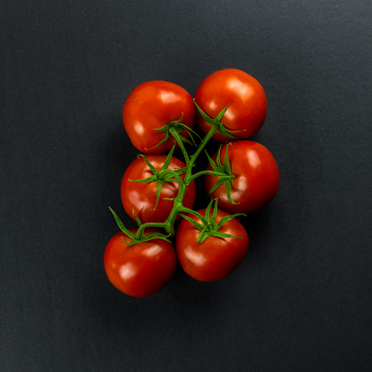 Fresh tomatoes with green leaves isolated on black serving platter.