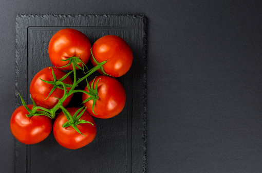 Fresh tomatoes with green leaves isolated on black serving platter.