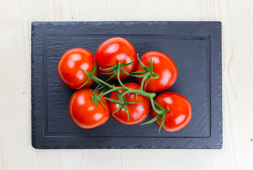 Fresh tomatoes with green leaves isolated on black serving platter.