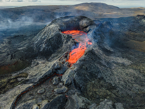 View into the crater of an active volcano with strong lava flow at the beginning of an eruption. Landscape on the Reykjanes Peninsula of Iceland. dark magma rock cooled around the volcanic crater