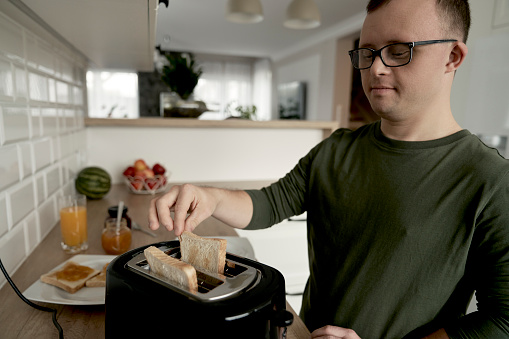 Caucasian adult caucasian man with down syndrome preparing toasts for breakfast