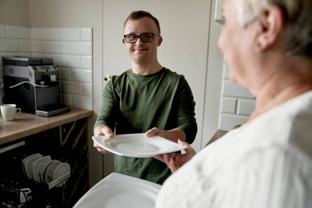 Caucasian adult man with down syndrome and his mother unloading dish washer at home stock photo