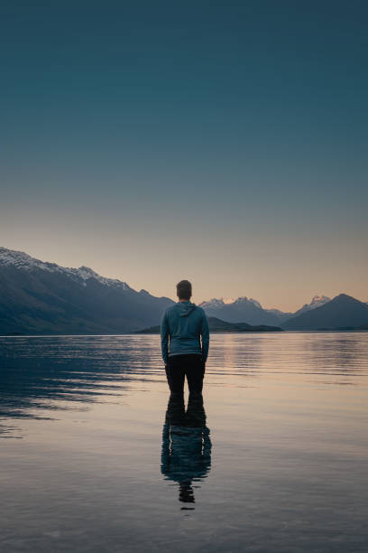 istock Man standing inside lake and looking at the mountainside at dusk 1439748536