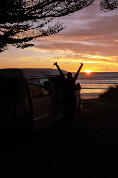 istock Man stretching arms next to his camper van at sunrise at the beach 1439748689