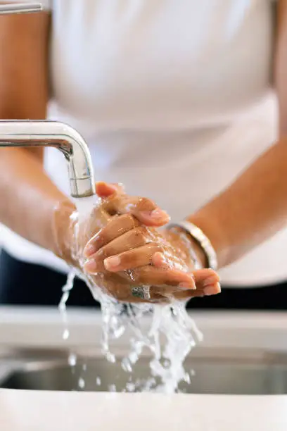 Photo of Latin American woman washing hands in the kitchen tap. Close up caption