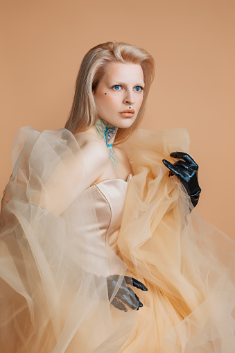 A beautiful blond alternative edgy female in a fantasy cream dress in a studio shot
