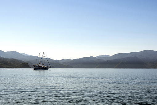 A single sailing tourboat at sea in Fethiye Turkey and a view of the mountains in the background.