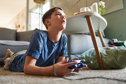 a boy lies on the carpet in the living room and plays video games