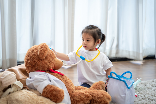 A happy Asian girl playing doctor or nurse listening a stethoscope to toy.