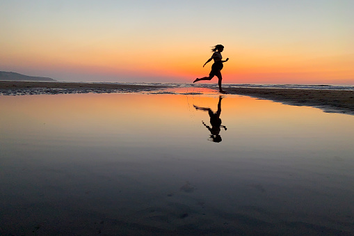 Picture perfect. A pregnant woman running on the beach in Spain. The orange sky makes a beautiful reflection.
