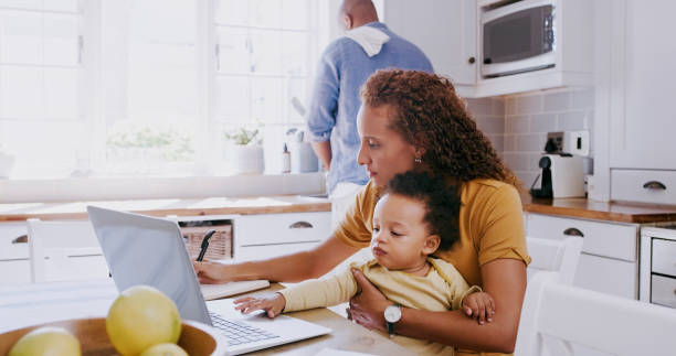 Family, baby and mother on laptop in kitchen working from home with father washing dishes. Love, care and freelancer, remote worker and mom multitasking, book writing and bonding with kid in house. stock photo