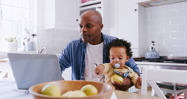 Work from home, laptop and father with baby working, typing or doing online research for child care, time management and finance planning. Remote work, child and black family dad in kitchen on his pc stock photo