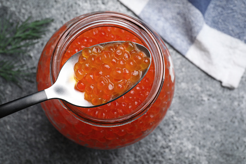 Taking delicious red caviar with spoon from jar on grey table, top view