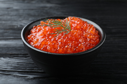 Bowl of delicious red caviar with dill on black wooden table