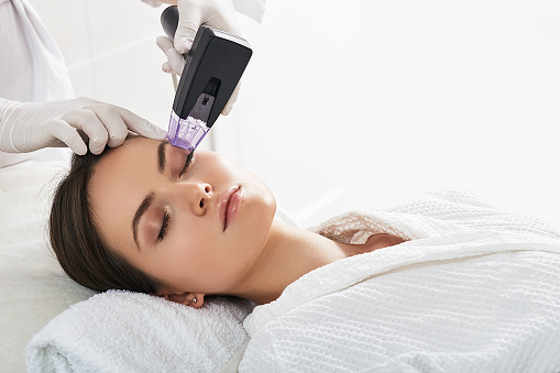 Mujer de cabello castaño recibe un procedimiento de levantamiento por radiofrecuencia alrededor de los ojos para el rejuvenecimiento de la piel de su cara en un centro de cosmetología estética photo