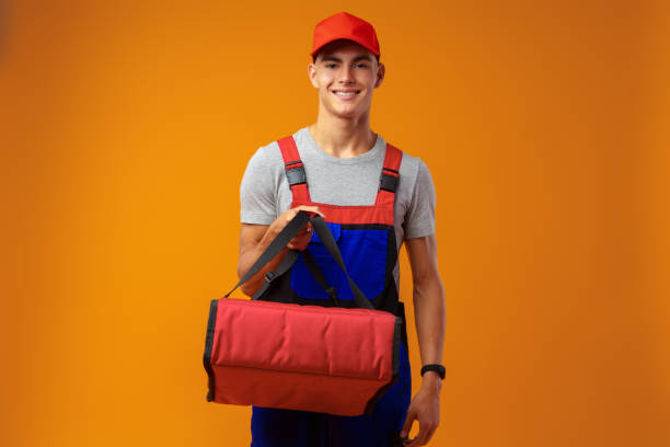 istock Young courier in uniform with thermo bag on yellow background 1439763251