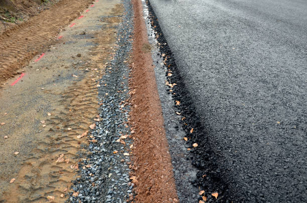 A newly built road, on the layer of which you can see successive layers of screed and asphalt coatings and penetration spraying. the edge is gradually shaped by earth at ditch, uncomplete, fall down , penetration, bitumen, abbreviation, work flow, renovation una carretera de nueva construcción, en cuya capa se pueden ver capas sucesivas de revestimientos de regla y asfalto y pulverización de penetración. el borde es gradualmente moldeado por la tierra en la zanja, incompleta, caída hacia abajo