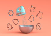 Metal bowl with electric mixer and cookie cutters on coral background