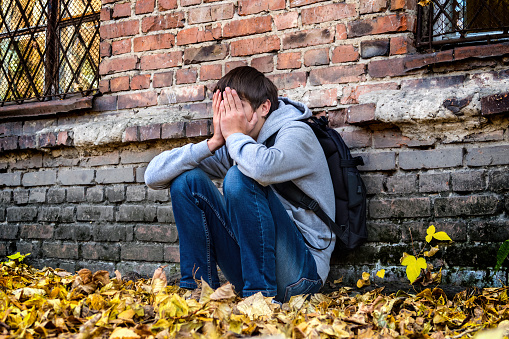 Sad Teenager sit near the Brick Wall of the Old House