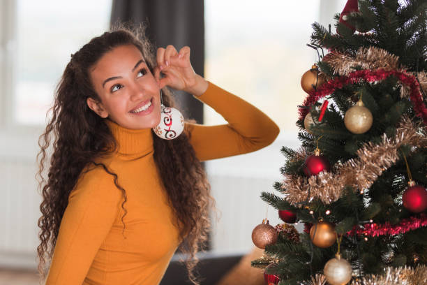 Cheerful young woman having fun and playing with Christmas balls from the Christmas tree, making earrings