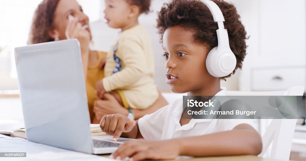 Laptop, online education and child with headphones listening in a video call for translation, language learning or audio kids subscription music. Black family kid on pc in kitchen for home school app 12-17 Months Stock Photo