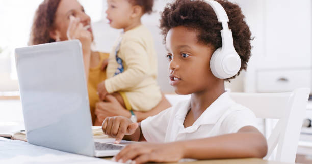Laptop, online education and child with headphones listening in a video call for translation, language learning or audio kids subscription music. Black family kid on pc in kitchen for home school app stock photo