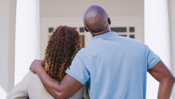 Real estate, new home and black people couple with outdoor property house hug together for investment, savings and mortgage loan. Behind of african man and woman looking or moving into a new house stock photo