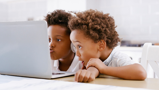 Children, laptop and elearning on internet and watching movie, video or playing education software games together at home table. Black kids or friends together for wow ebook on teaching website