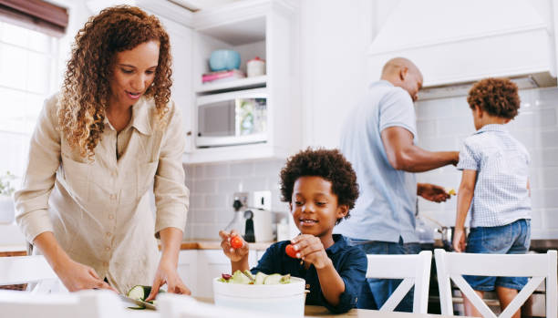 Cooking, kitchen and black family parents with children prepare food ingredients, supply or consumables for dinner, lunch or brunch. Fruit salad, wellness health and nutritionist mom help makes meal stock photo