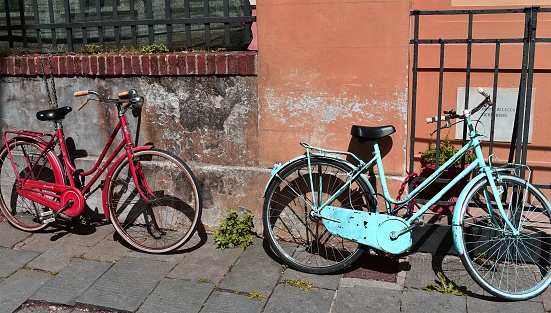 The rusty red and blue bicycles leaning on weathered building walls and metal gate