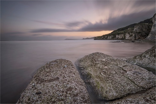 A breathtaking view of rock formations on the shore against sunset sky, long exposure