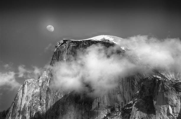 Grayscale of a cloud covered mount peak with the moon in the background