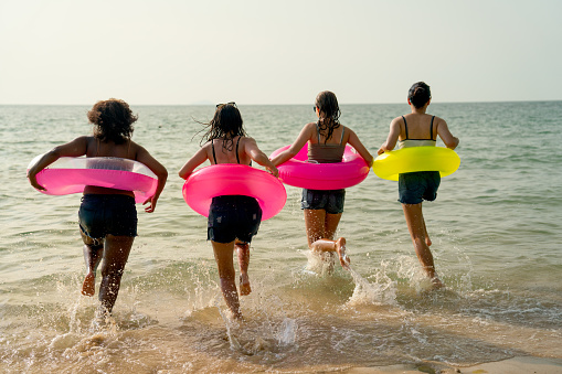 Back of teen girls with swimming rings run into the sea with warm light of sunset during holiday or relax time of vacation at beach.