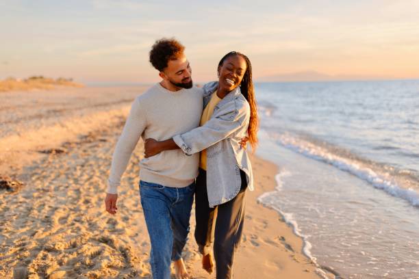 pareja caminando en la playa durante la puesta de sol - couple love autumn romance fotografías e imágenes de stock