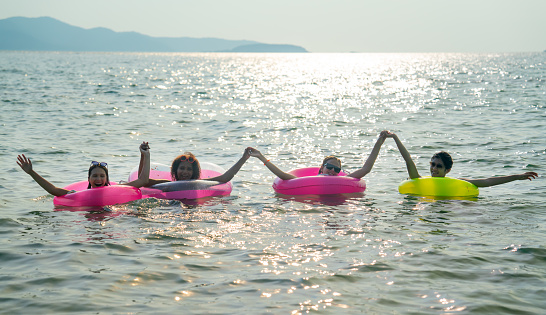 Group of teenage girls with swimming rings hold their hands together and float with fun in the sea with warm light reflect to the water as background.