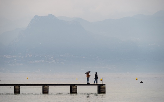 Sirmione, Italy – May 07, 2022: A beautiful shot of a couple standing on a pier on a rainy day in Lake Garda, Italy