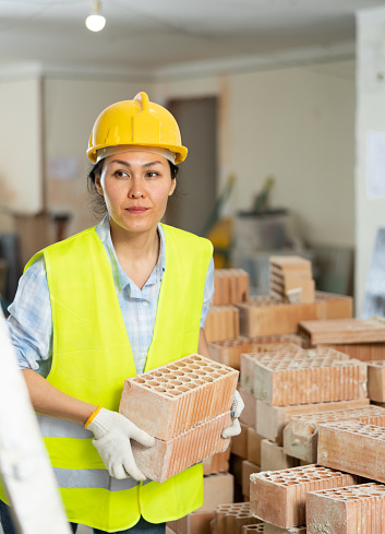 Young adult woman builder working at renovating object carrying bricks at construction site