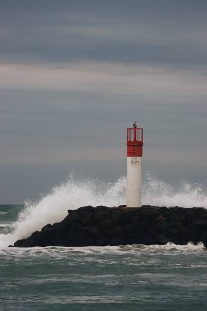 istock Vertical shot a white lighthouse  with a red top and a wave hitting it 1439773626