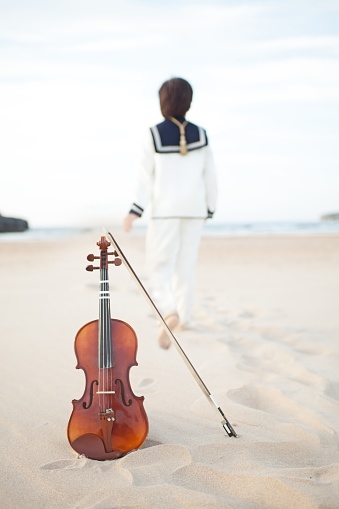 A vertical shot of a violin on the beach with a child walking away on the blurry background - musical concept