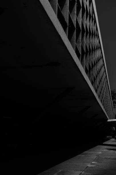 istock Vertical greyscale low angle shot of a modern building under a cloudy sky 1439775419