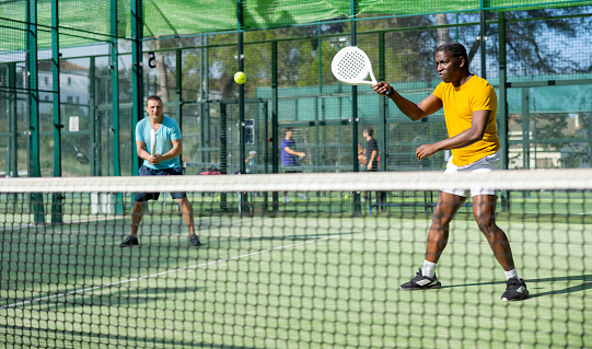 African american male player ready to hits the ball while playing padel on hard court