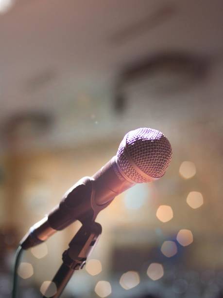 istock Vertical shot of a microphone on a stand under the lights with a blurry background and bokeh effect 1439776110