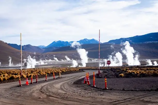 Photo of Road with traffic cones and a scene of El Tatio Geyser with smoke in the background, Chile