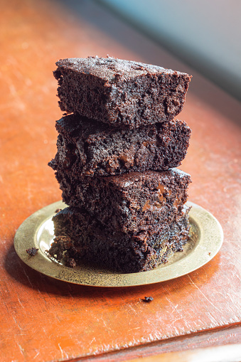 A stack of freshly baked chocolate brownies with chocolate chips on a plate on a wooden table. There is copy space or room for text around the brownies.