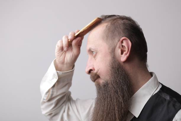 istock Man with a long beard and a mustache brushing his hair with a grey wall on the background 1439777862