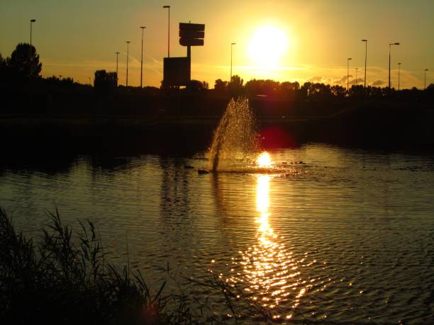 Amsterdam, Netherlands – July 21, 2012: A fountain spraying water in a water tank in Amsterdam, Netherlands at sunset, with a yellow, orange sky.