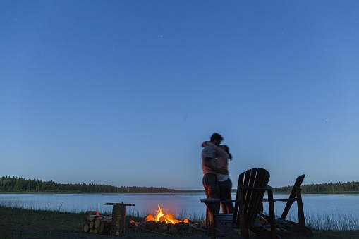 silhouette of a couple hugging next to a bonfire at dusk next to a lake