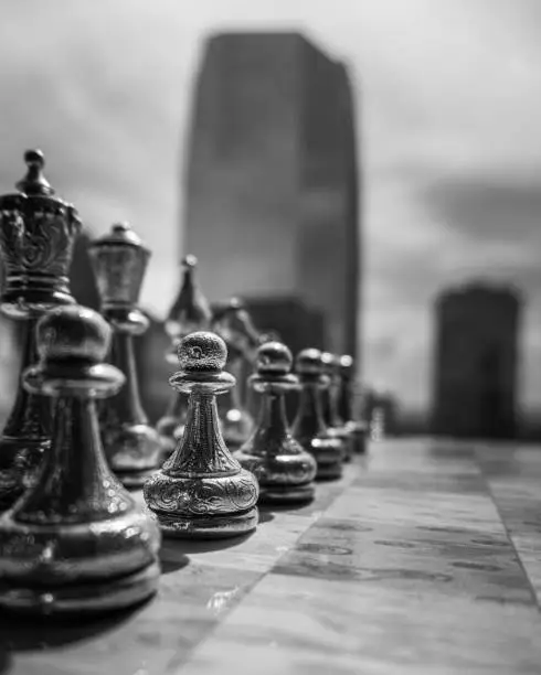 A vertical grayscale shot of chess figurines with buildings in the background in Denver