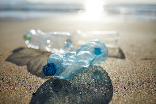 Close-up of empty plastic bottles on shore. Abandoned waste is on sand. Garbage is polluting beach.